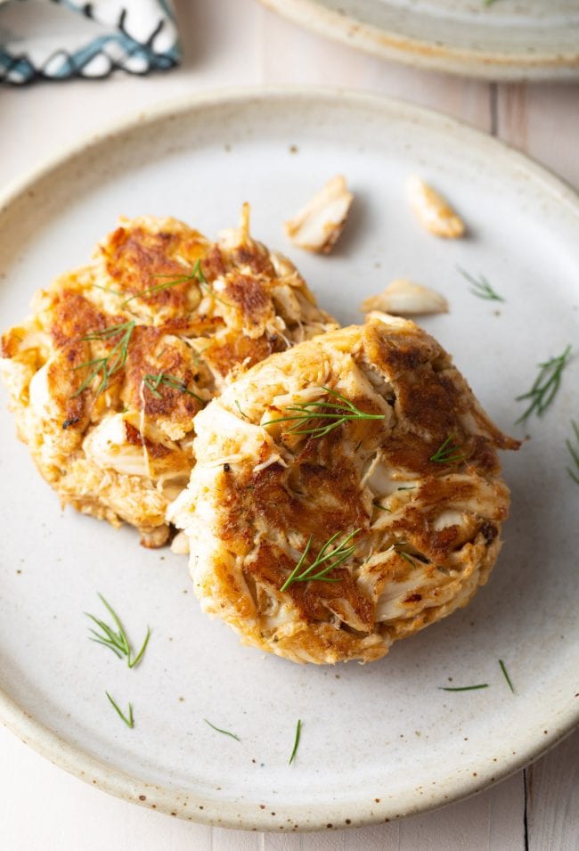 Two crab cakes plated with fresh dill as a garnish. 