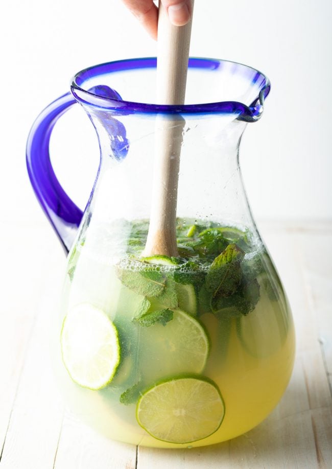 A wooden spoon is mixing all of the mojito ingredients together in the pitcher. 