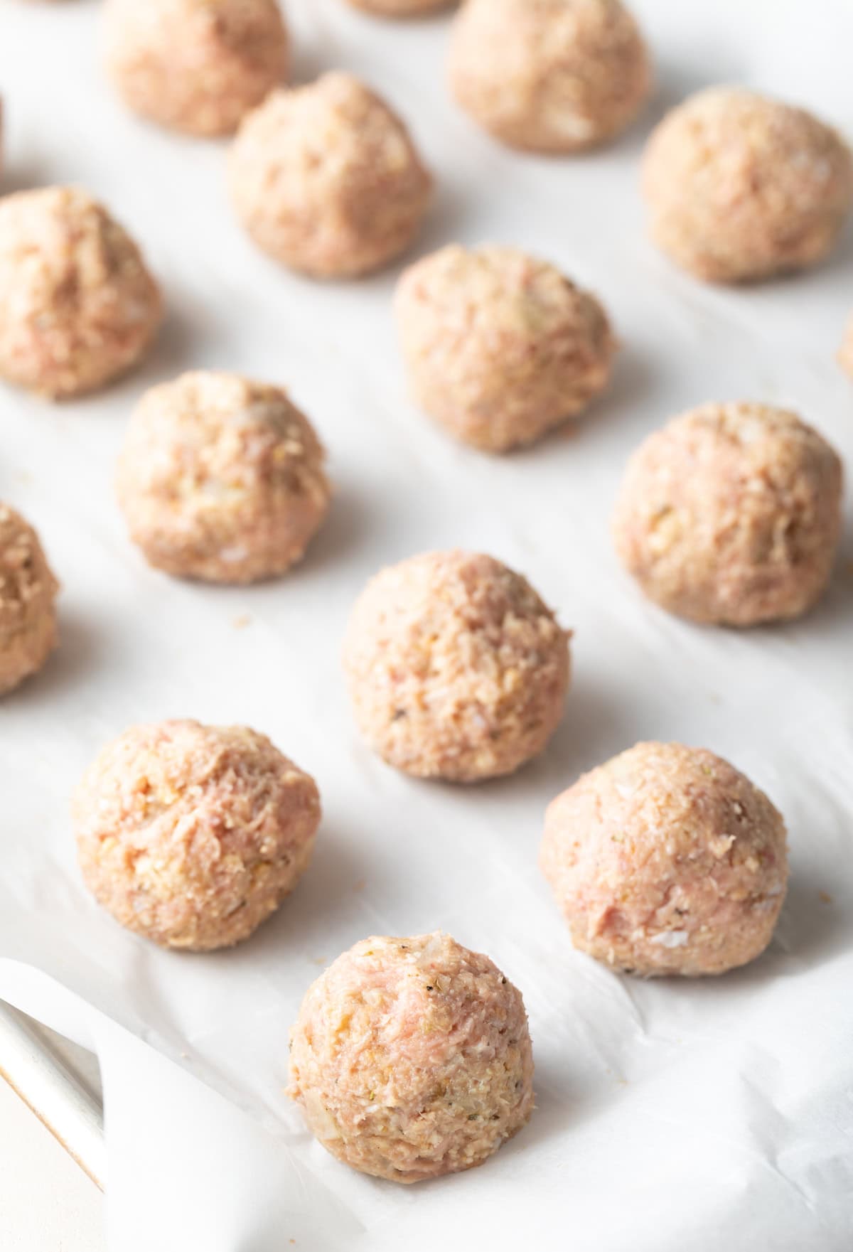 Uncooked turkey meatballs lined up on a baking parchment-lined baking sheet.
