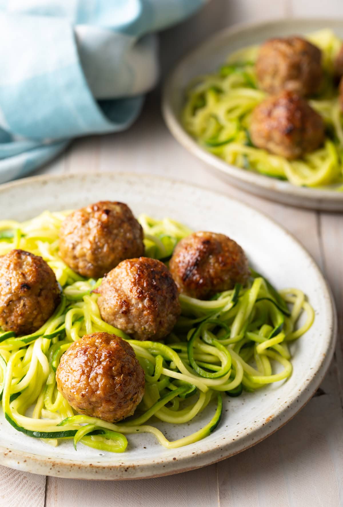A side-on view of two stone plates of turkey meatballs on top of a tangle of cooked zucchini noodles.