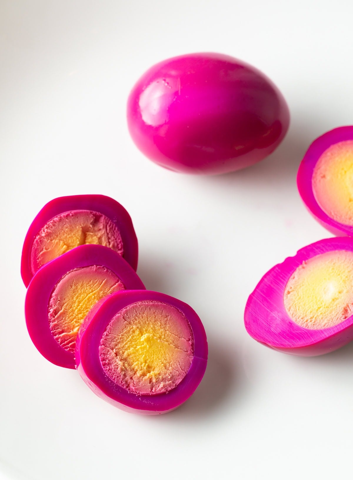 Pink hard boiled egg sliced into three rings, on a white background with another whole egg and a third egg cut in half.