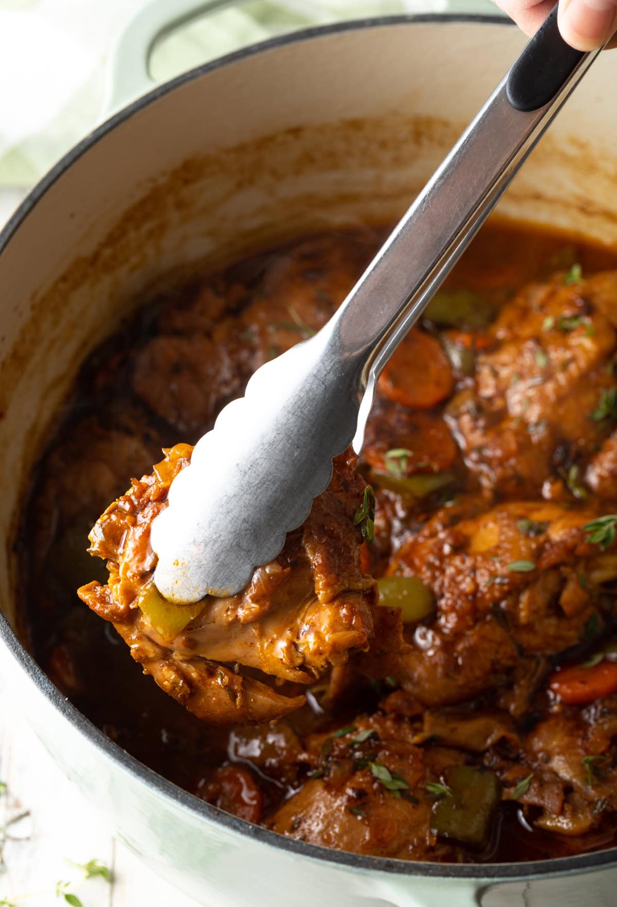 Pot filled with ready to serve stew and a tong removing a piece of chicken.