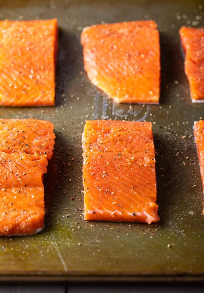 Closeup of uncooked seasoned salmon fillets on a baking dish.
