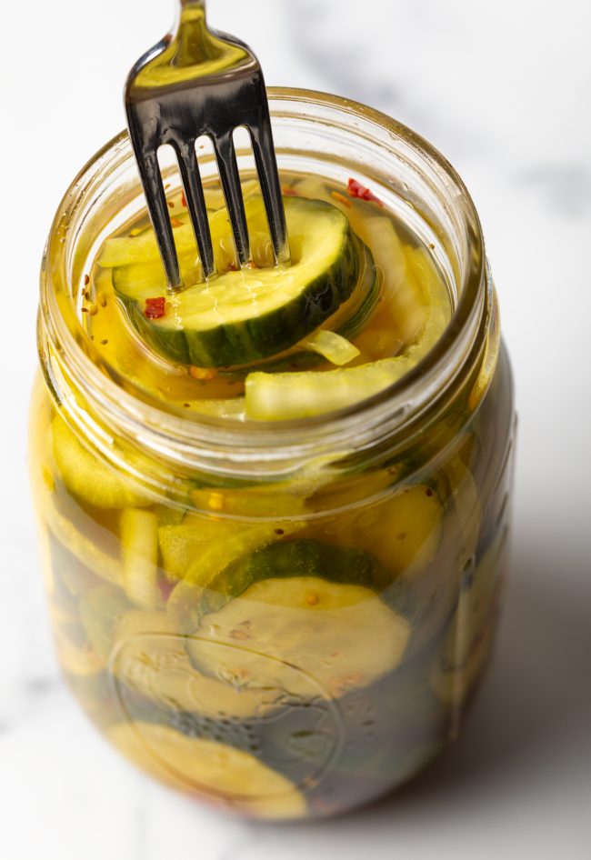 using a fork to get a sweet pickle slice from a jar