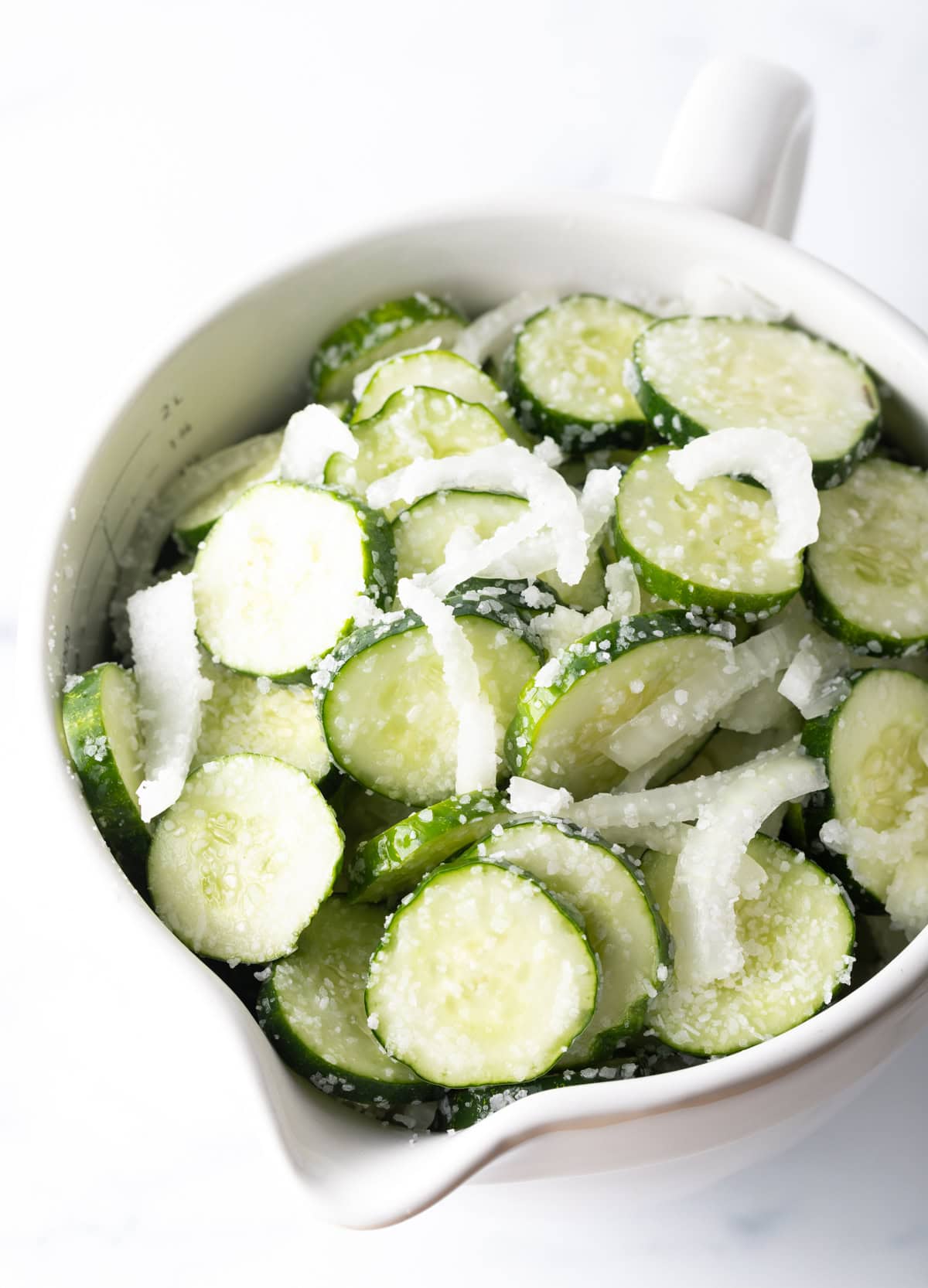 White bowl with sliced cucumbers and white onion.