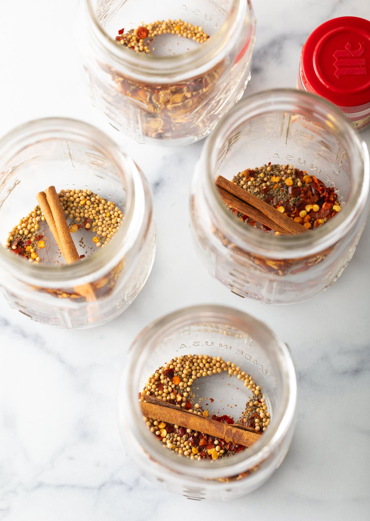 Four glass jars with cinnamon sticks and mustard seeds.