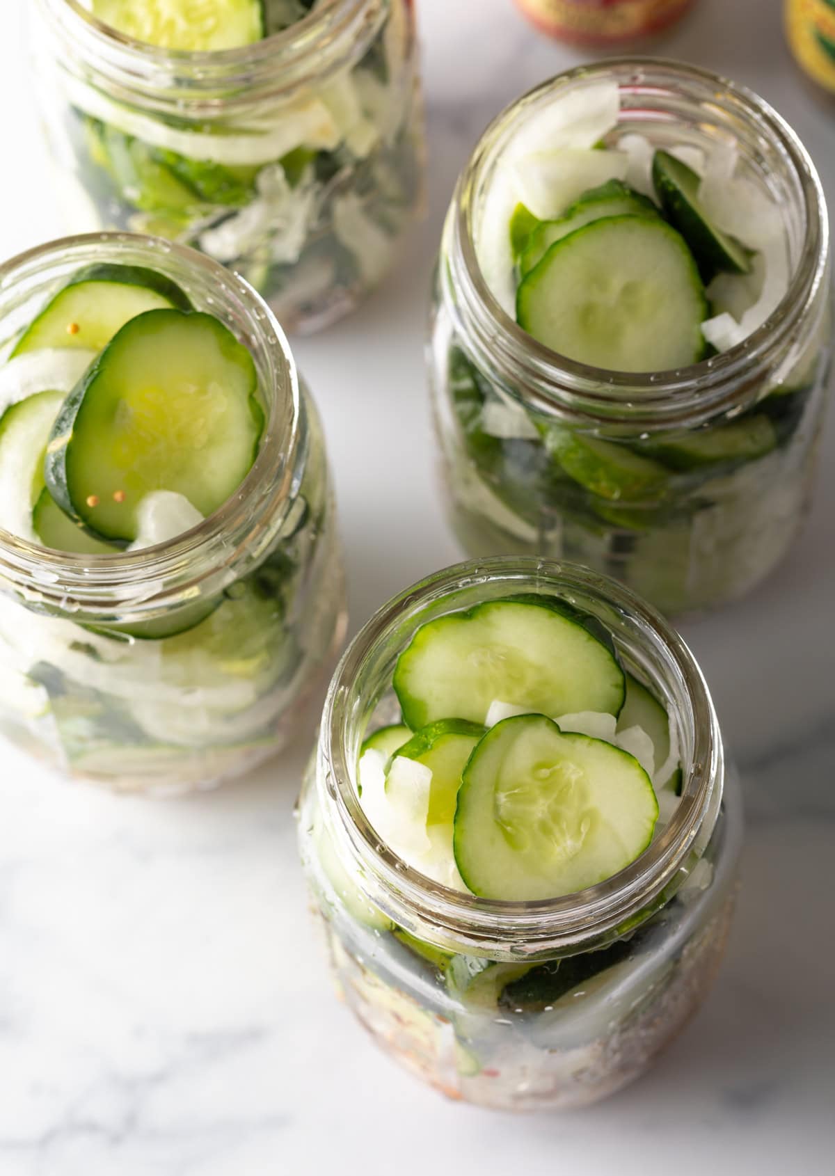 Four glass jars filled with cucumber slices and white onion.