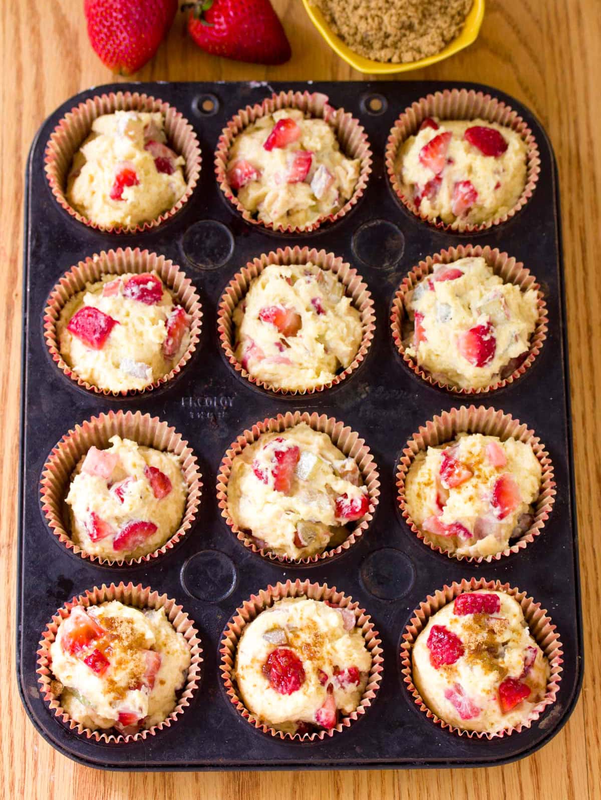 A pan of raw strawberry rhubarb muffin batter in paper liners.