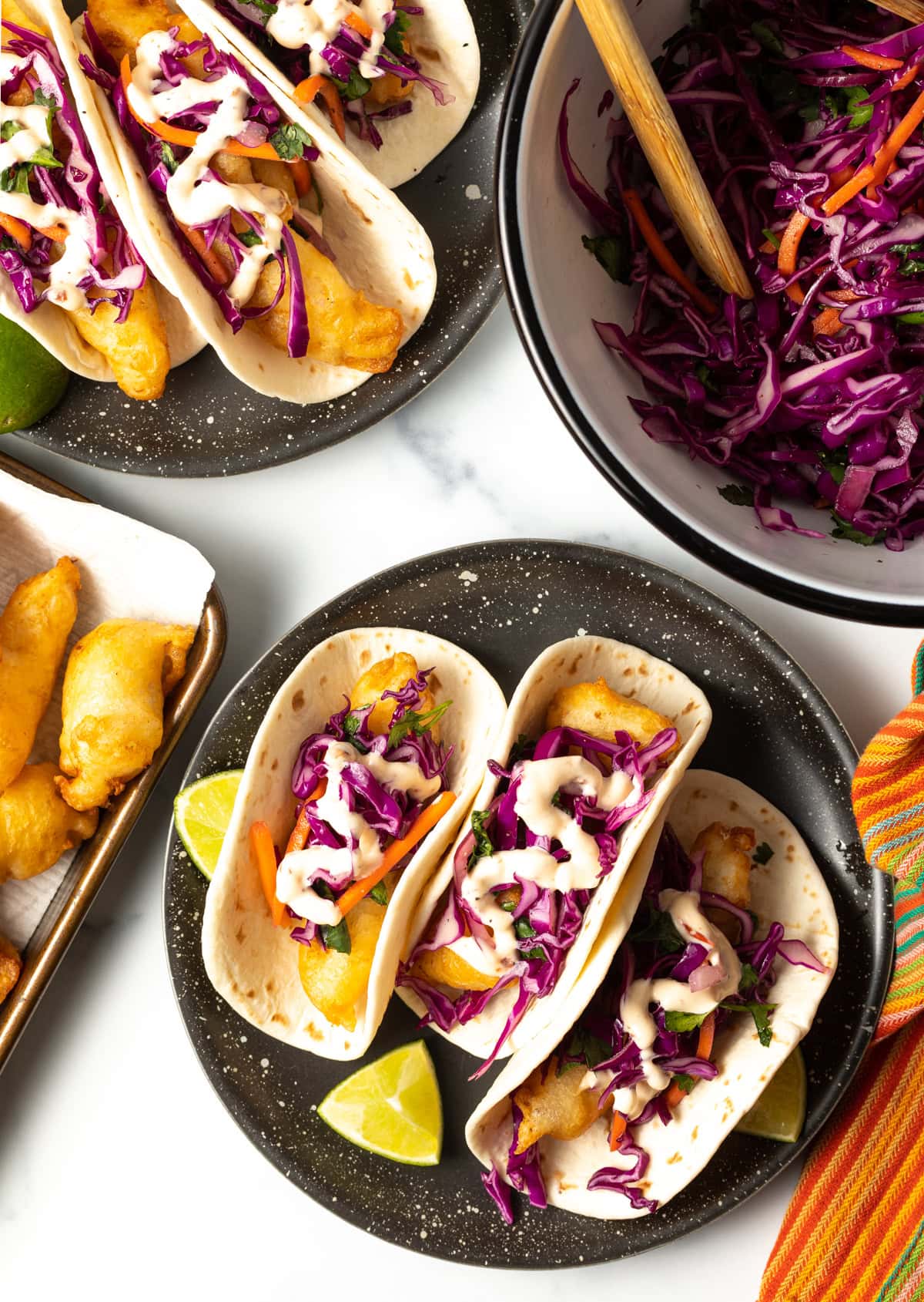 overhead view of 3 fried fish tacos with more fried fish, slaw, and baja sauce on the sides. 