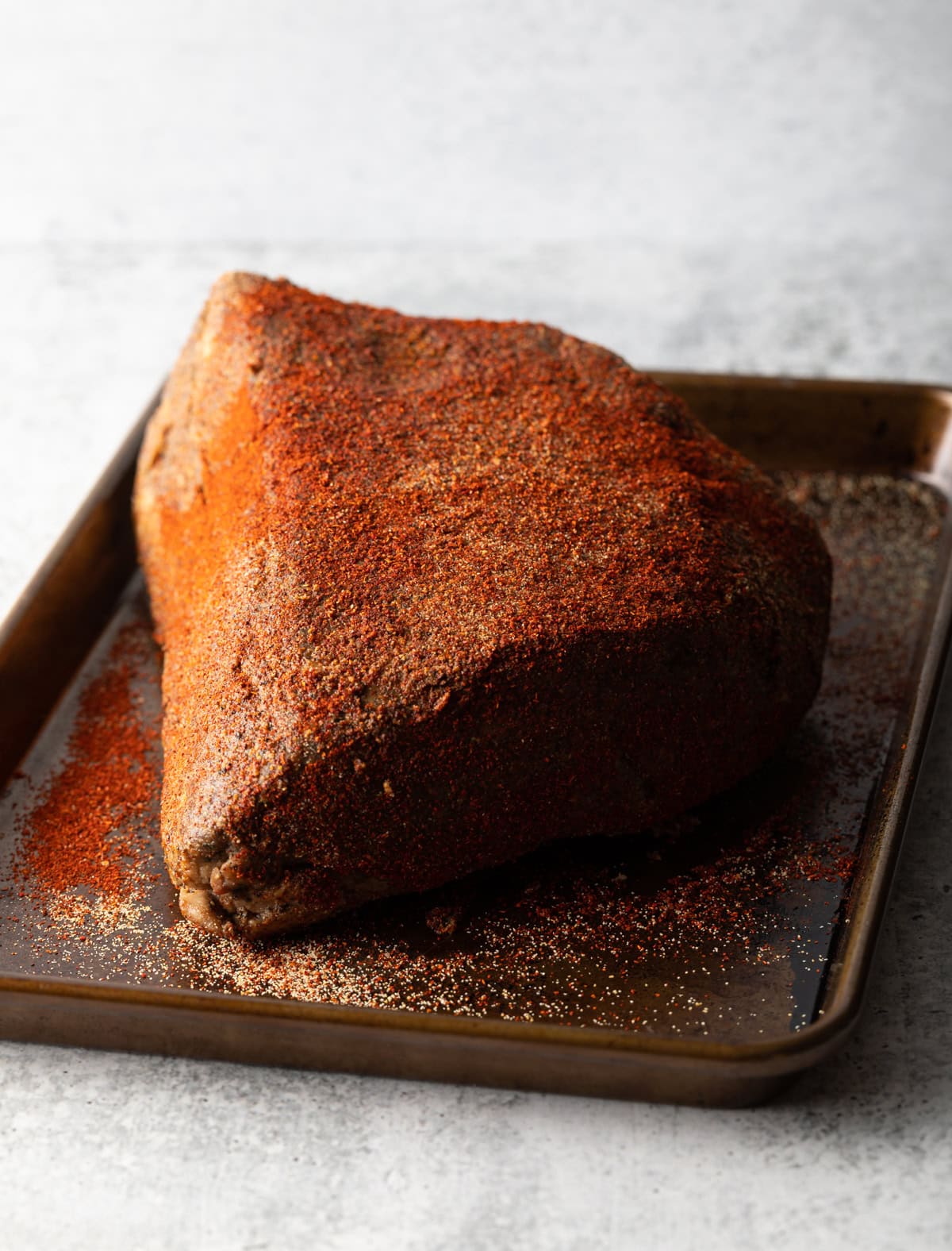 A piece of beef brisket on a baking sheet coated in dry rub.