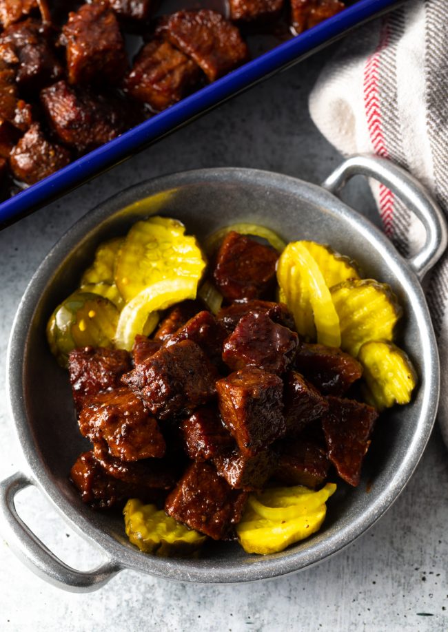 a bowl of burnt ends in bbq sauce with pickles