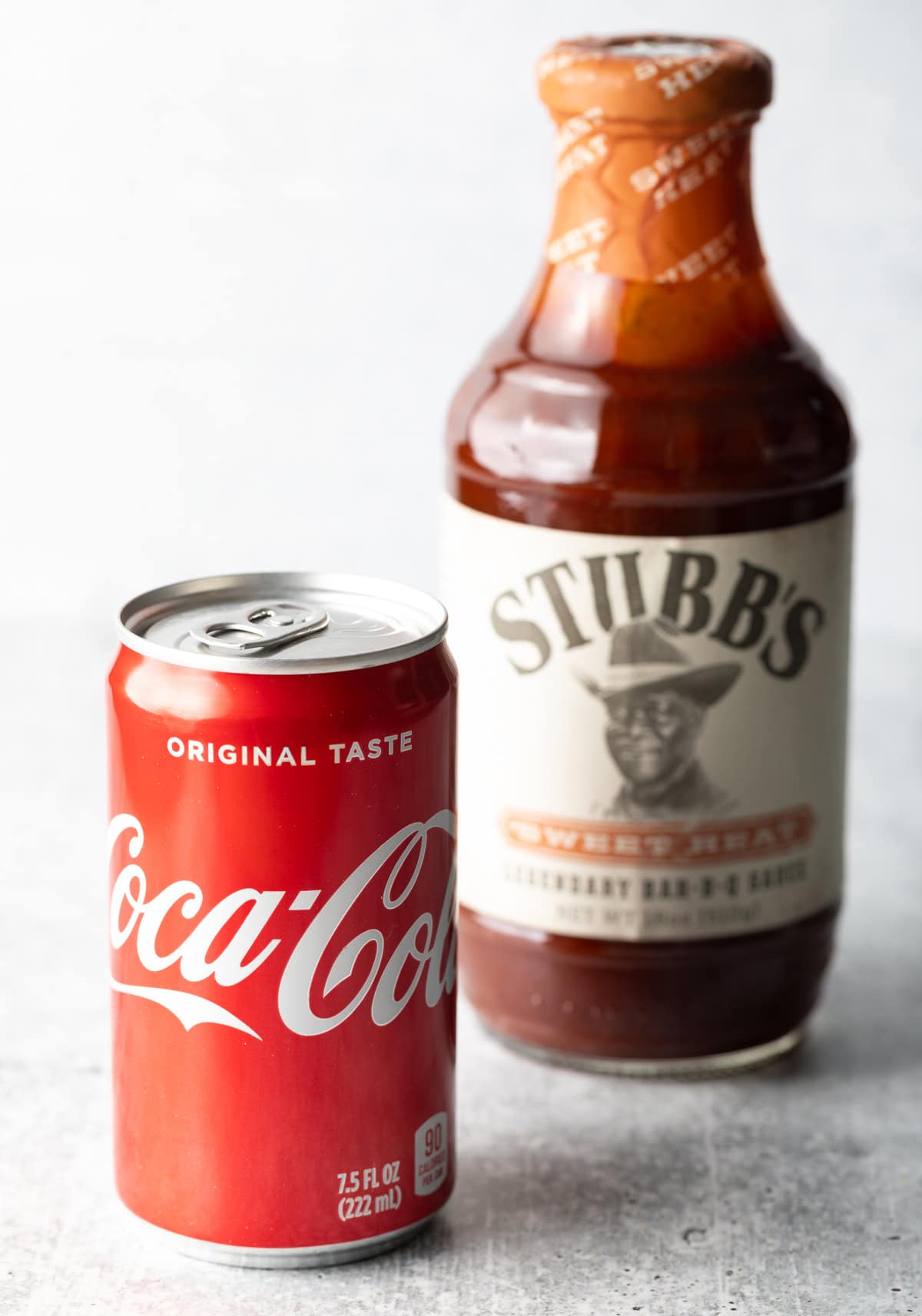 A can of coke with a bottle of Stubbs barbecue sauce in the background.