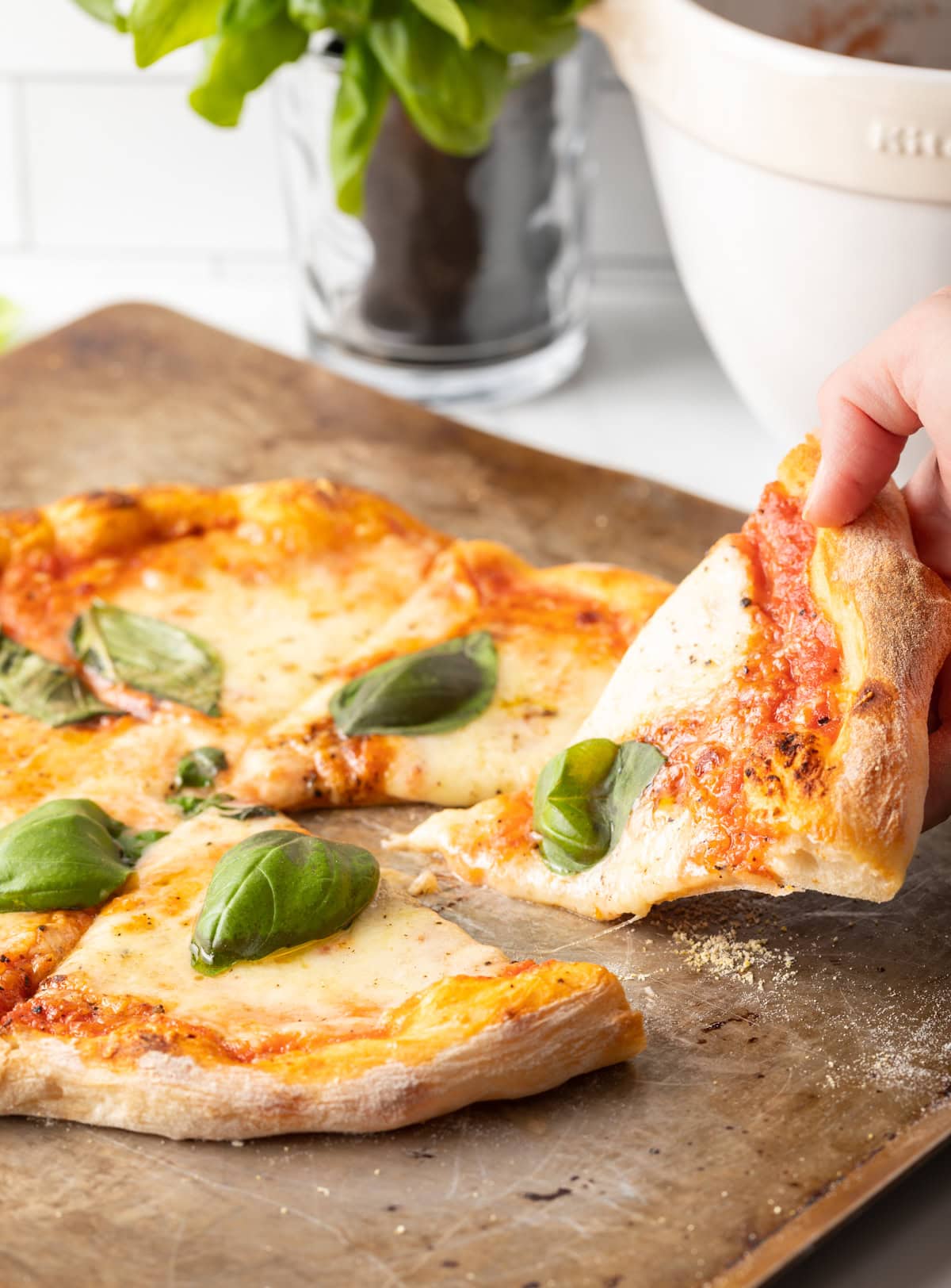 Hand taking a slice of baked Neapolitan pizza with fresh basil leaves.