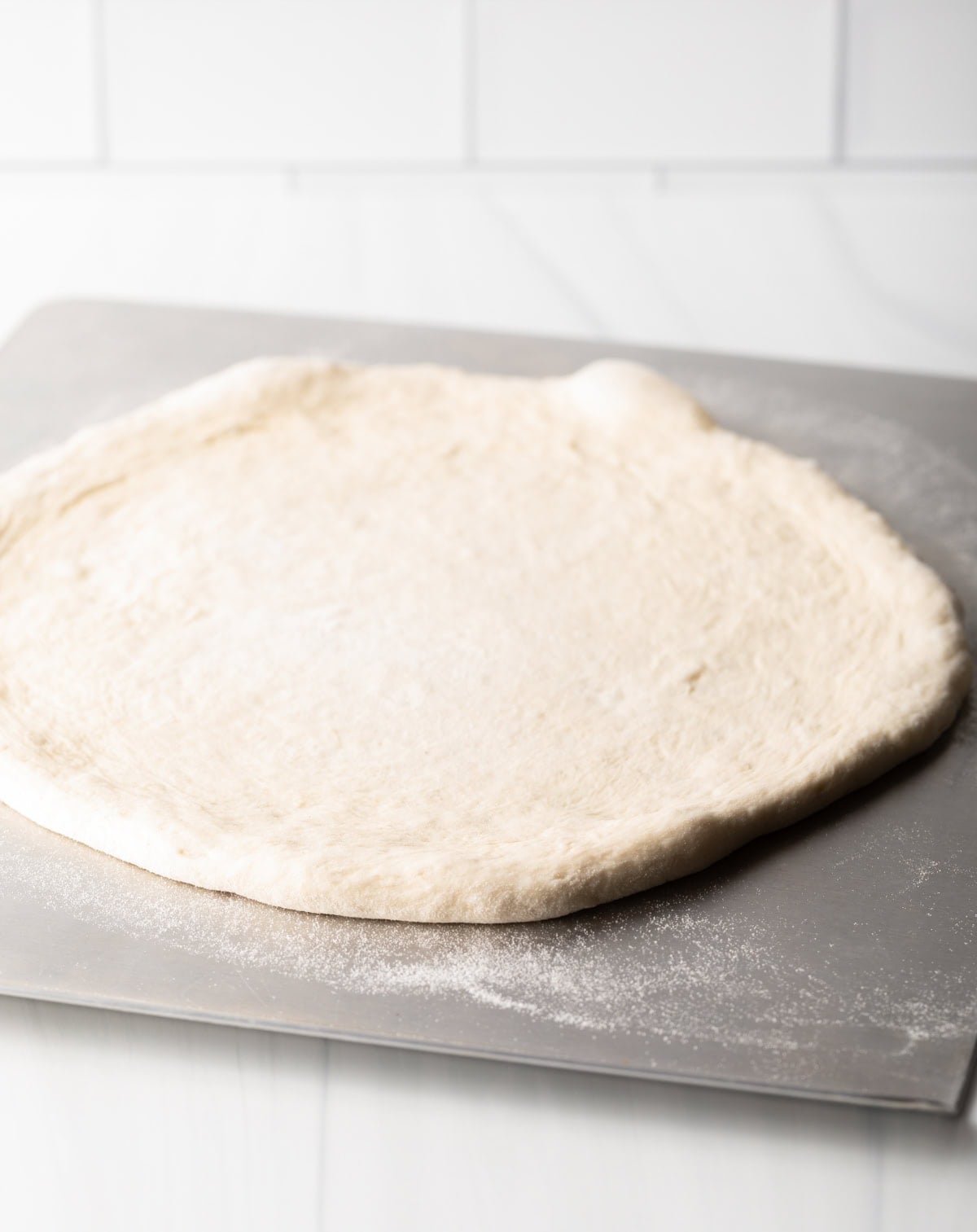 A circle of Neapolitan pizza dough spread on a metal baking sheet.