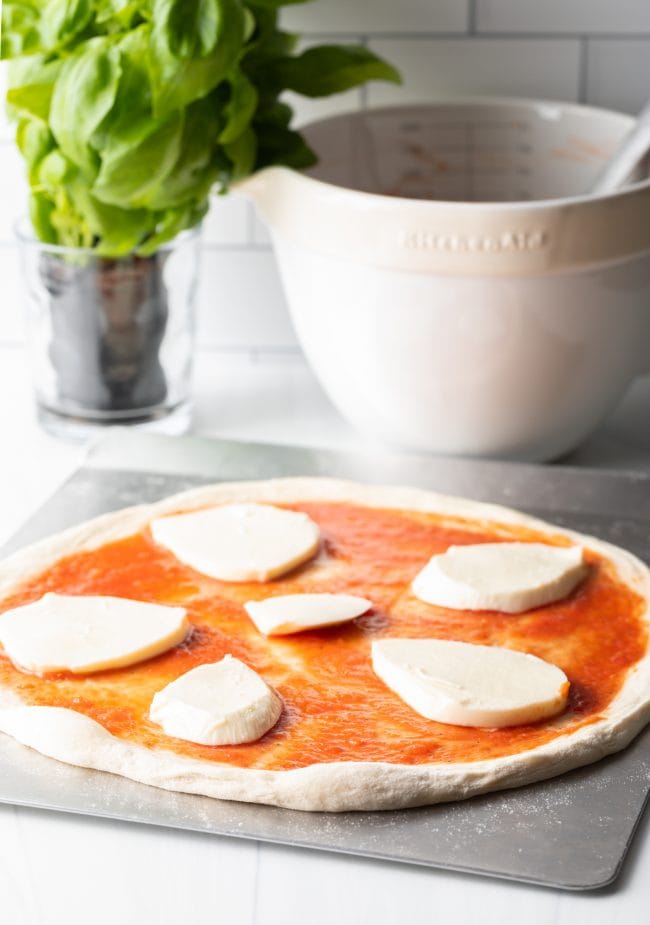 Large circle slices of mozzarella cheese on unbaked pizza.