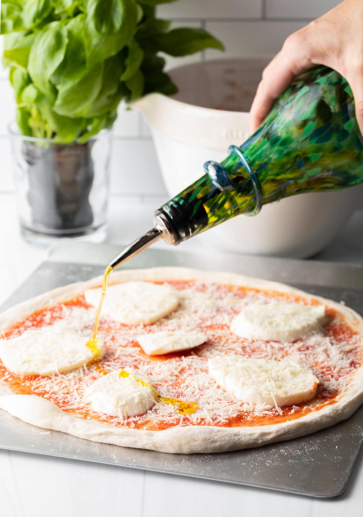 Drizzling olive oil over slices of mozzarella cheese on an unbaked pizza.