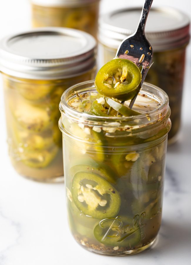 fork lifting a pickled jalapeno from a jar