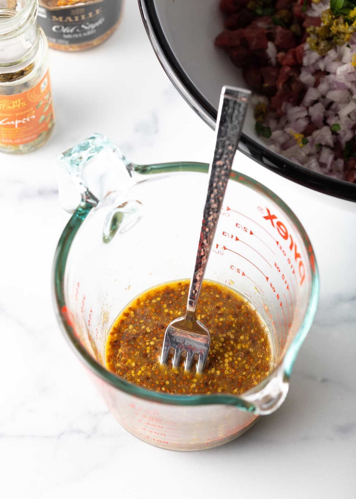 Jug of mixed mustard dressing with a fork resting in it.