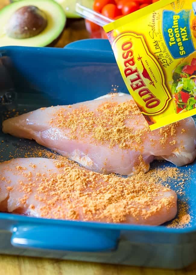 Raw chicken breast in a platter being seasoned with Old El Paso Taco Seasoning.