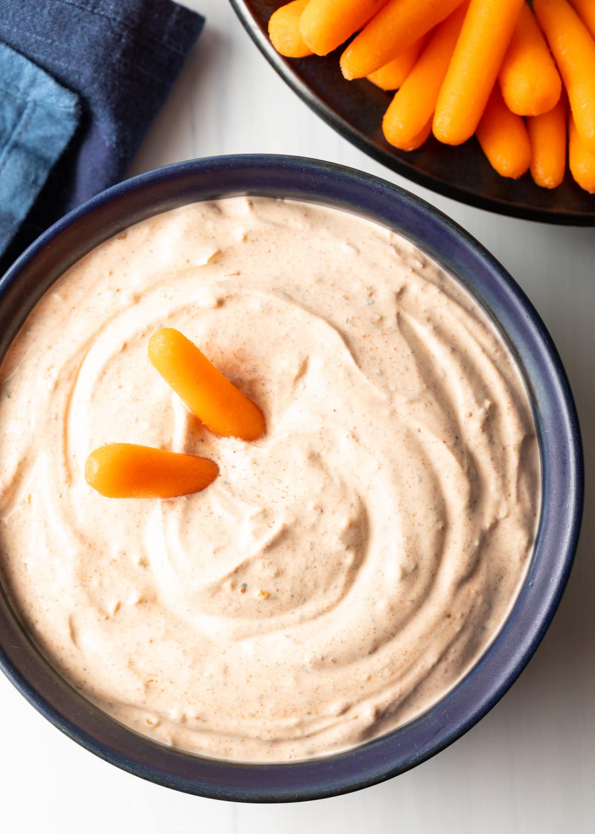 top overhead view blue bowl with creamy 3 ingredient taco dip, bowl of carrots to the side and 2 carrots in the dip