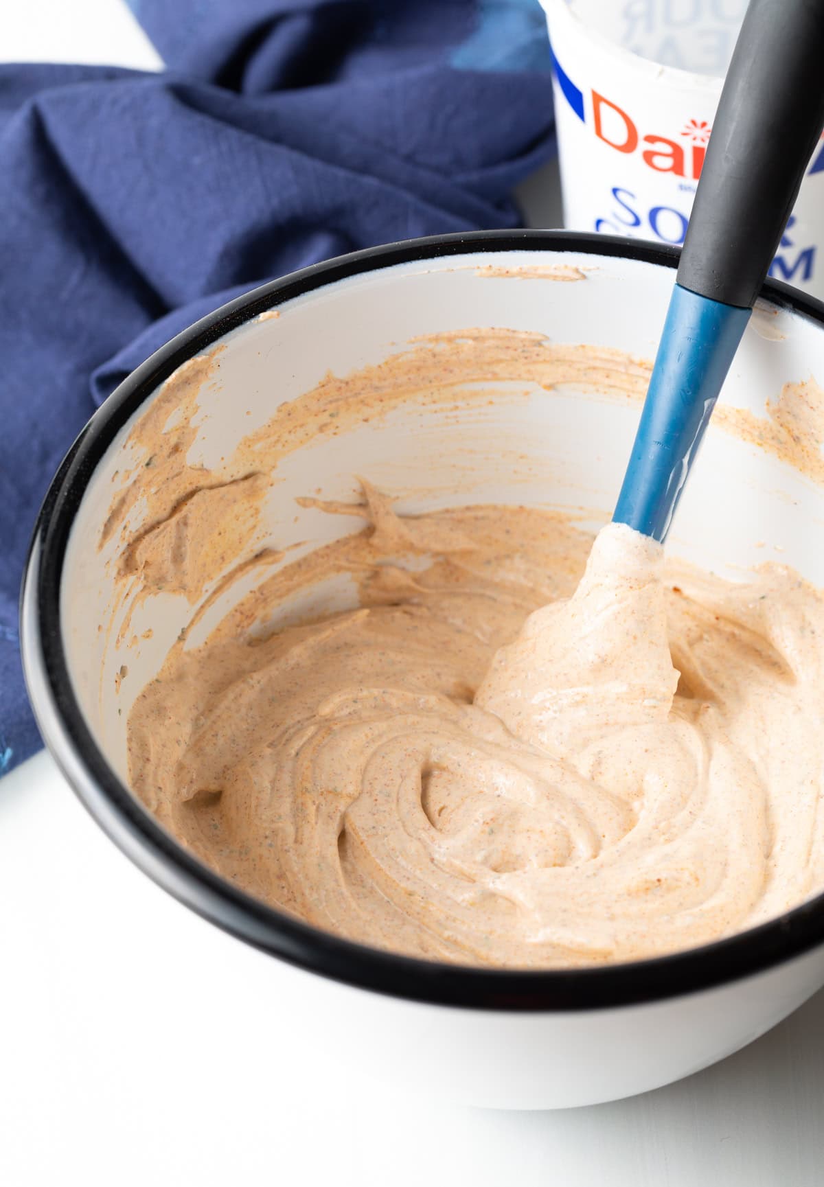 making the magic taco dip recipe with 3 ingredients together in a mixing bowl with a blue spatula