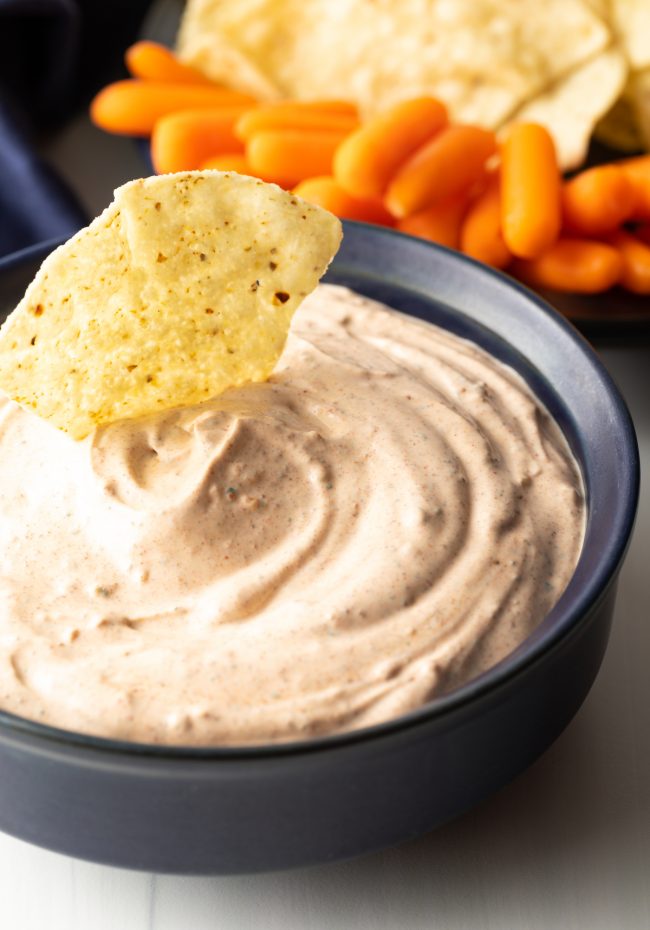 close up view of blue bowl with taco dip, tortilla chip stuck in dip