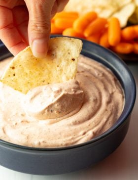 Hand using a tortilla chip to scoop taco dip from a black bowl.