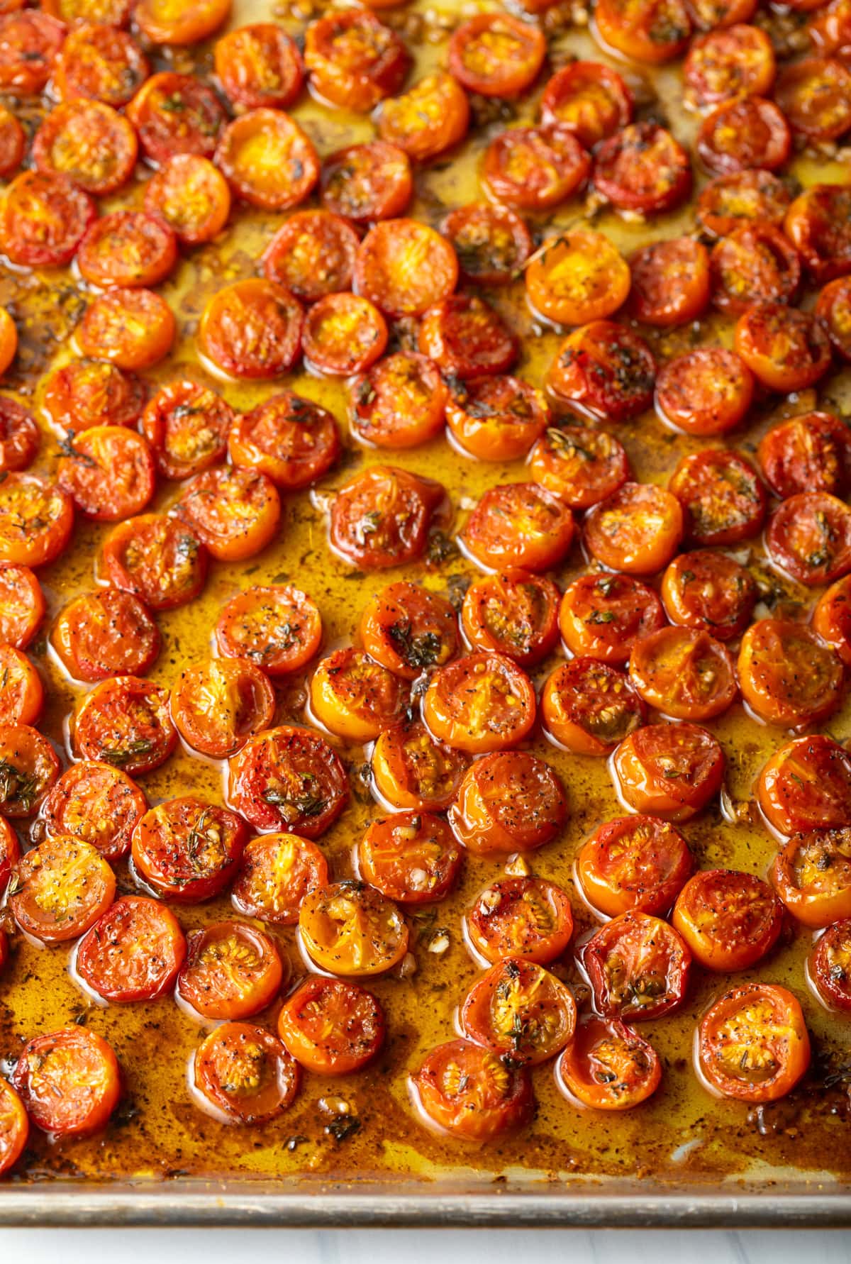Seasoned, roasted cherry tomatoes are arranged on a baking sheet.