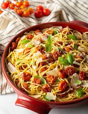 A bowl filled with roasted cherry tomato pasta topped with parmesan and fresh basil.
