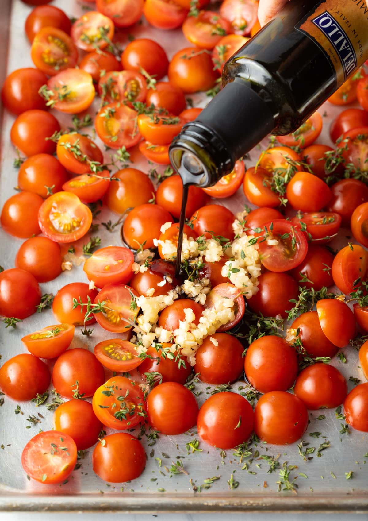 Halved cherry tomatoes topped with minced garlic and herbs, with balsamic vinegar being poured over.