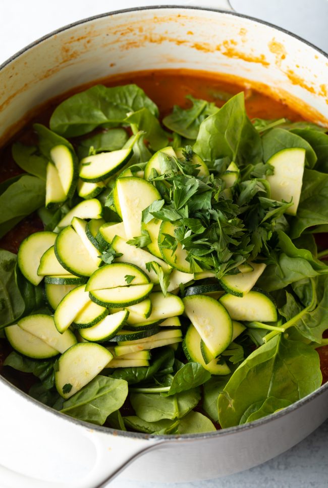 adding zucchini, fresh spinach and herbs to the soup pot