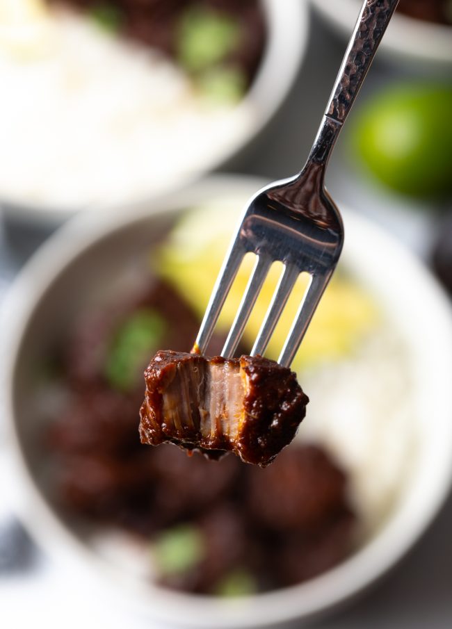 fork holding piece of red chile simmered pork with bite