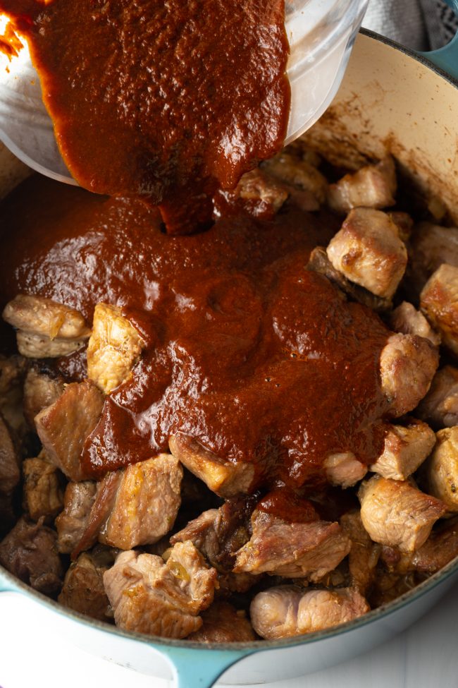 adding the smoky sauce to the chunks of seared pork in the pot