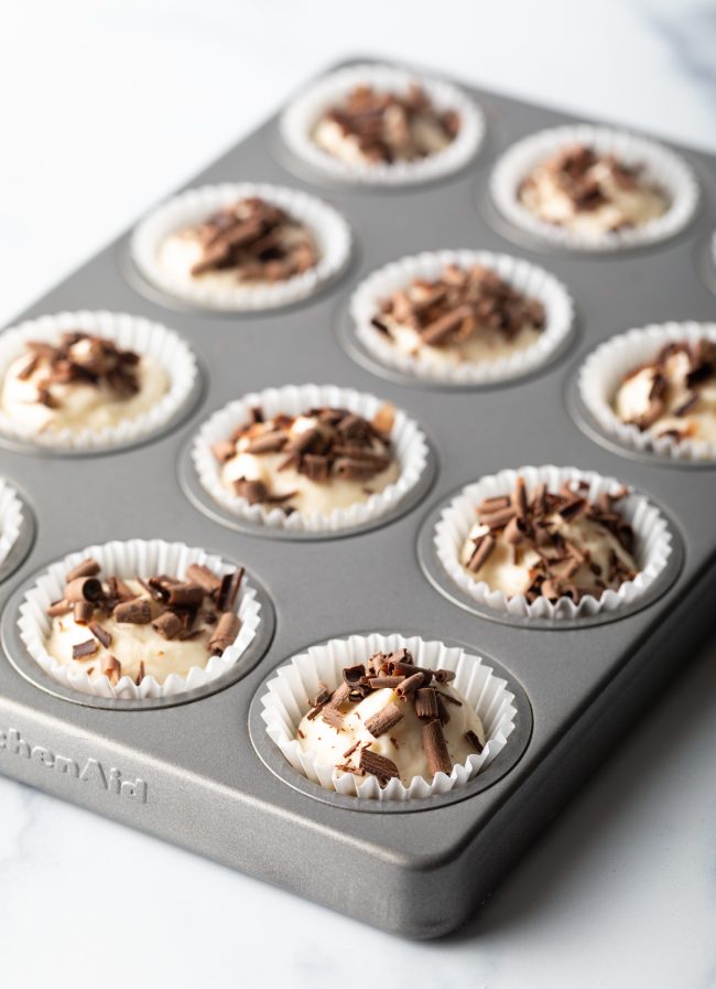 mini muffin tin with white paper liners filled with keto cheesecake bites topped with chocolate shavings
