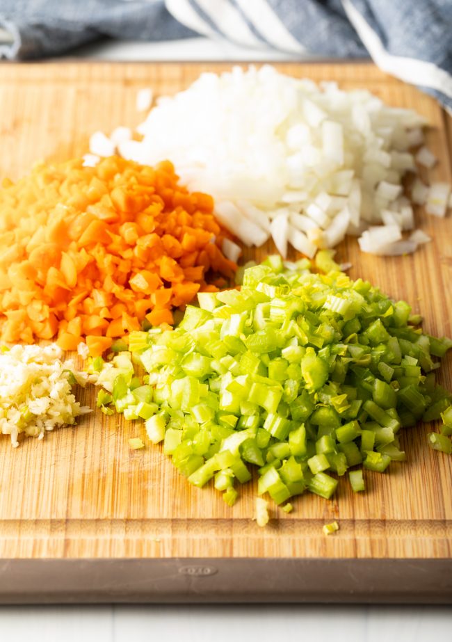 wood cutting board with piles of chopped celery, carrot, onion and garlic to make easy rigatoni bolognese recipe