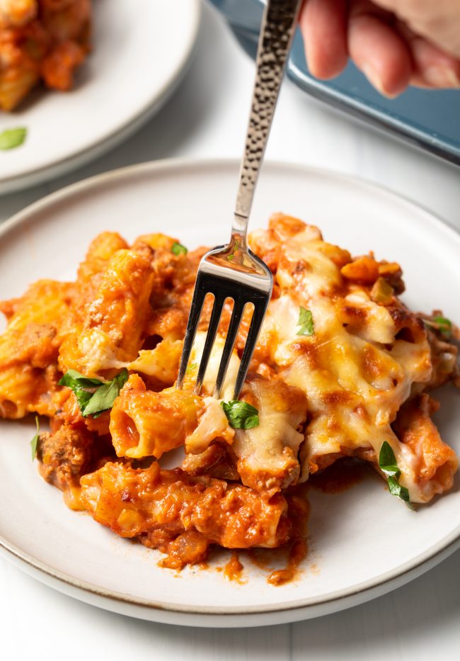 fork taking a bite of rigatoni pasta with bolognese sauce and cheese