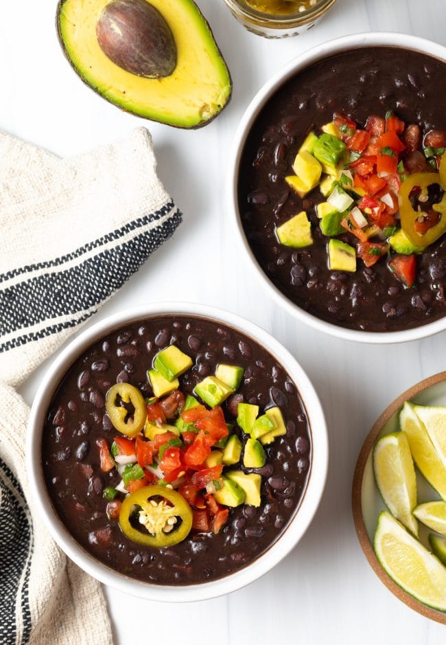 Easy Black Bean Soup - Top down two white bowls of black bean soup topped with slices of jalapenos, chopped avocado, and pico de gallo.