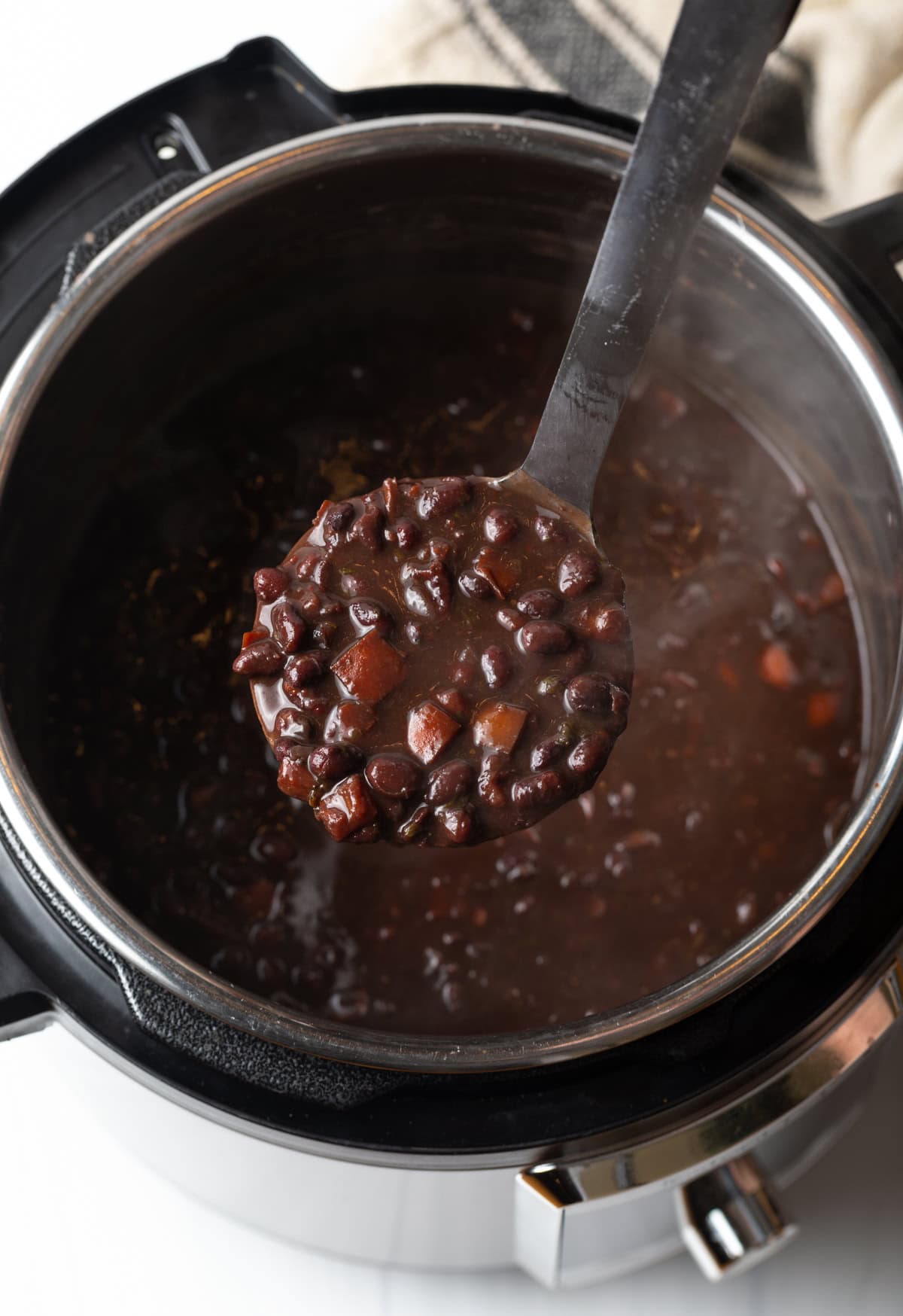 Ladle with black bean soup over an instant pot.