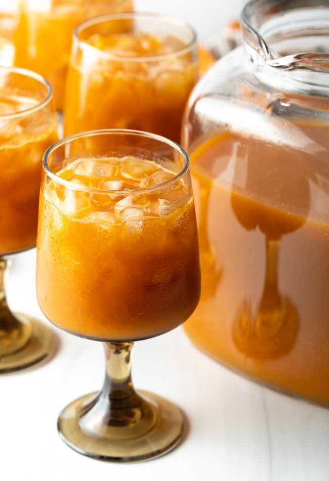 glass of iced juice with pumpkin puree and fruit over ice, next to a pitcher of juice