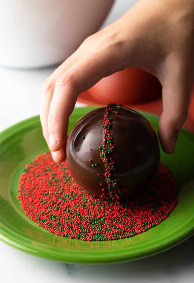rolling hot chocolate ball on a plate of green and red sprinkles