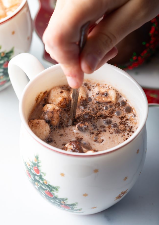 hand stirring mug of melted hot cocoa ball with mini marshmallows