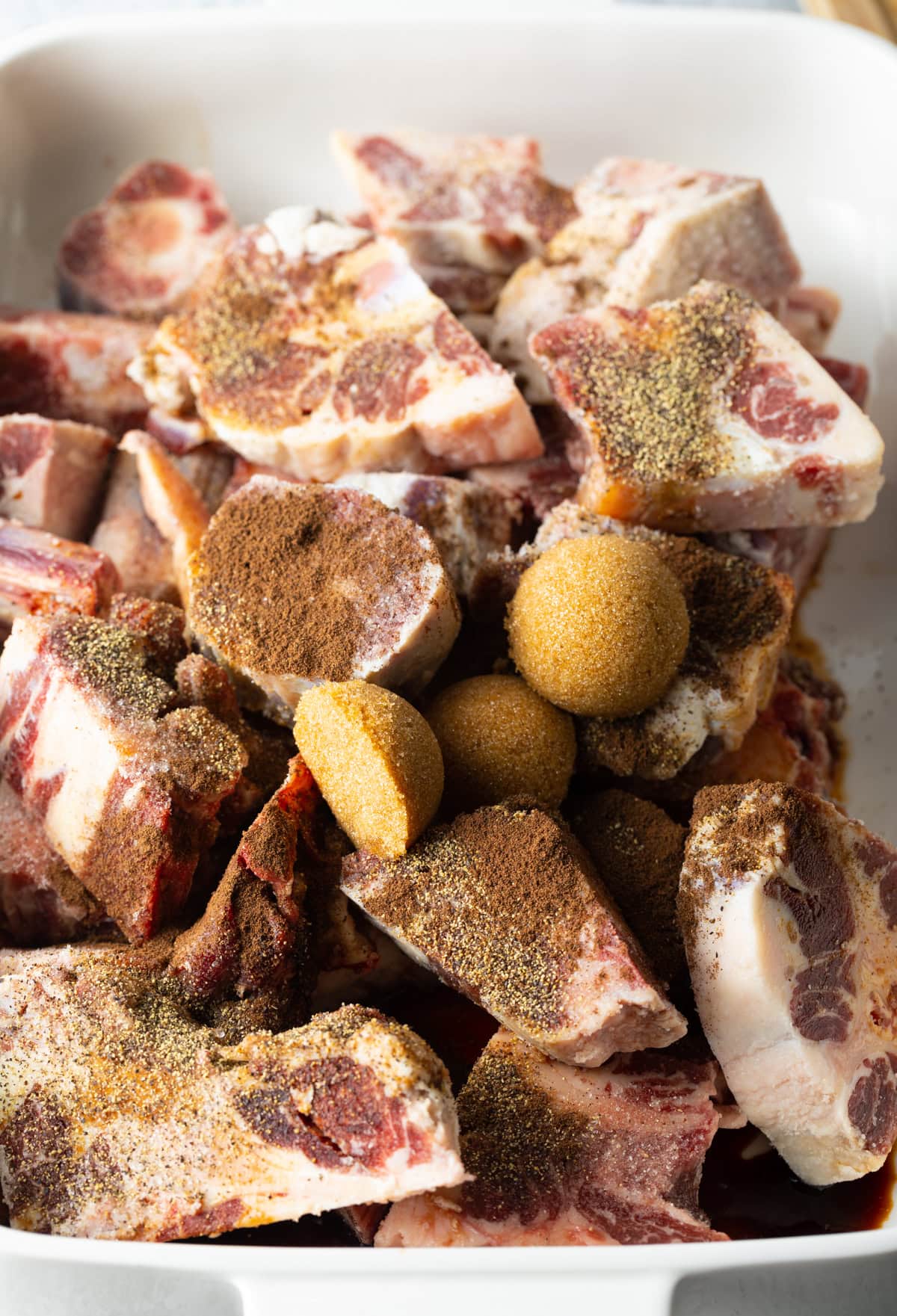 Raw pieces of oxtail in a large cooking pot, seasoning with spices and brown sugar.