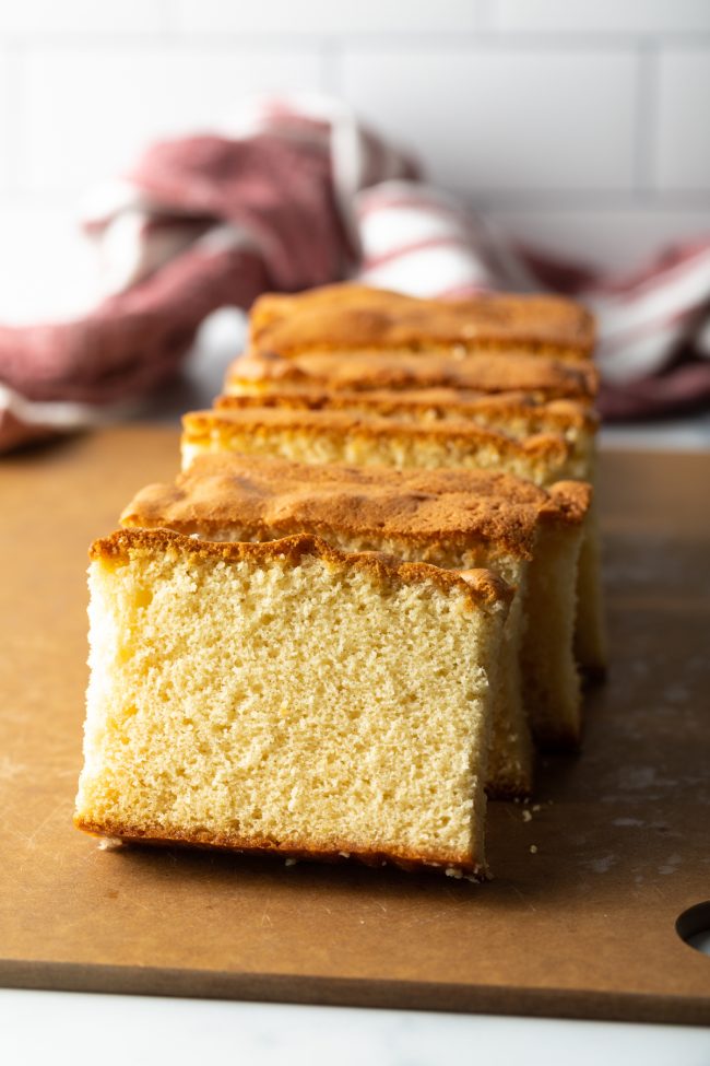 slices of castella Japanese sponge cake stacked against each other resting on a brown cutting board