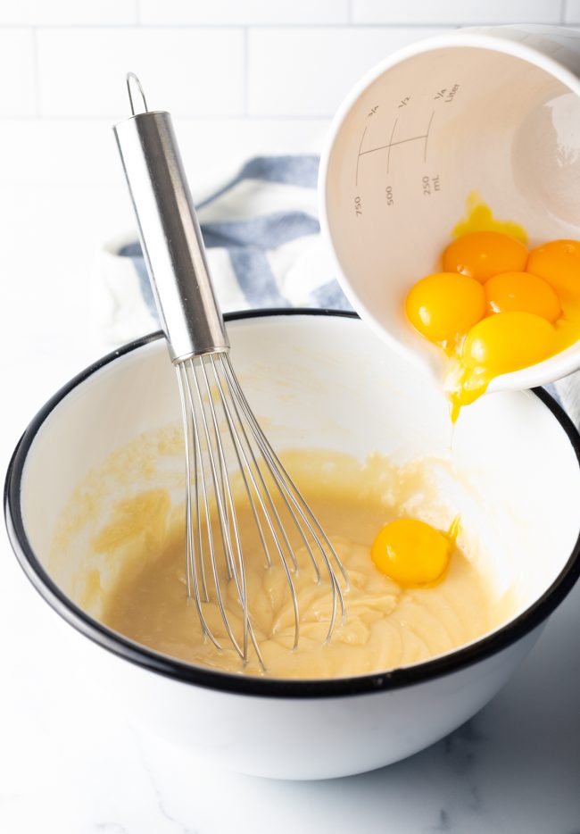 adding eggs to a batter in a bowl with metal whisk