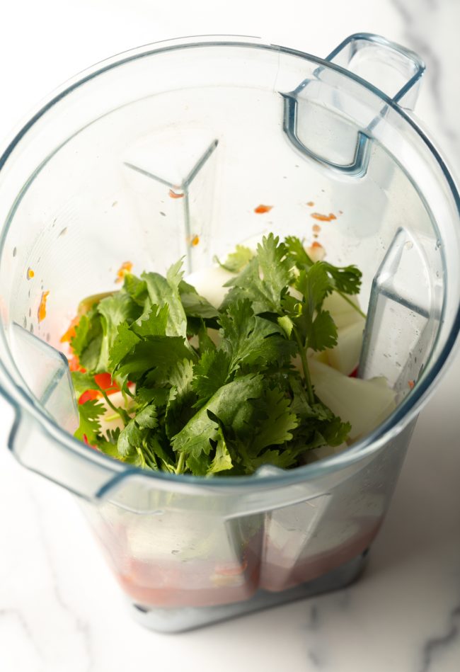blender jar top view with cilantro added to other ingredients