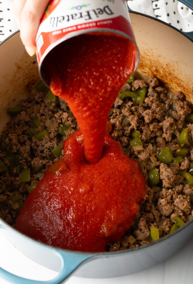 pouring a can of tomato sauce into the pot