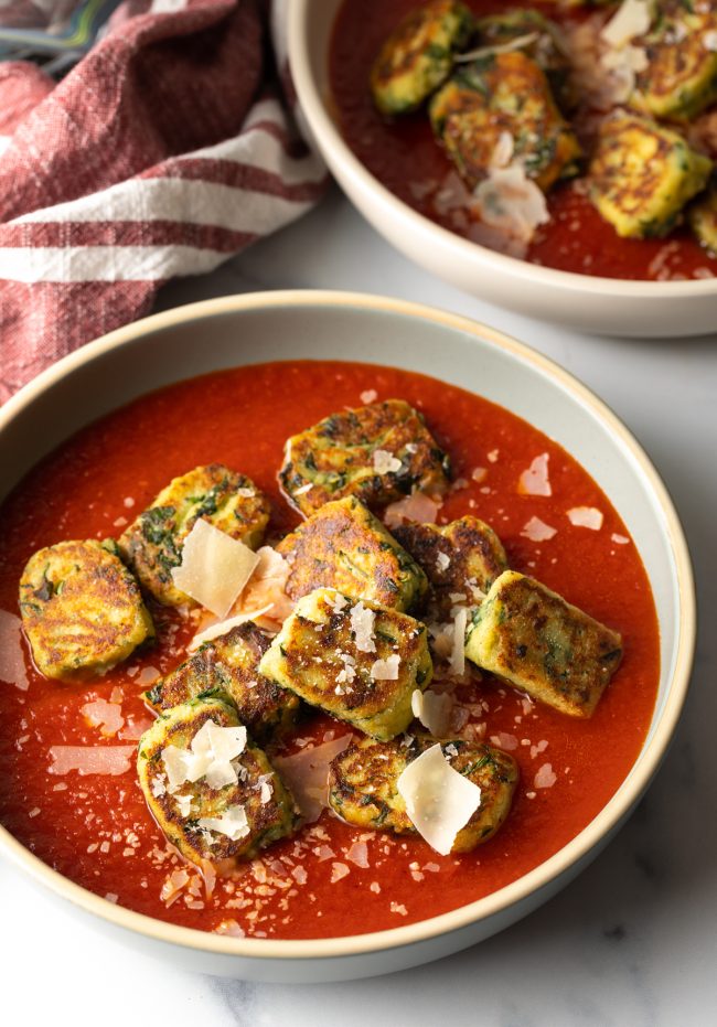 two bowls of ricotta gnudi with tomato sauce and shaved parmesan