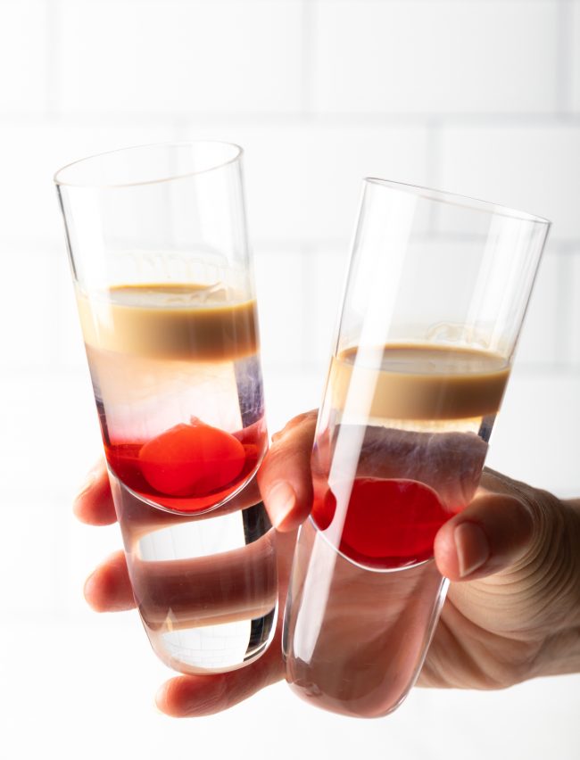hand holding two shot glasses with slippery nipple cocktails in each
