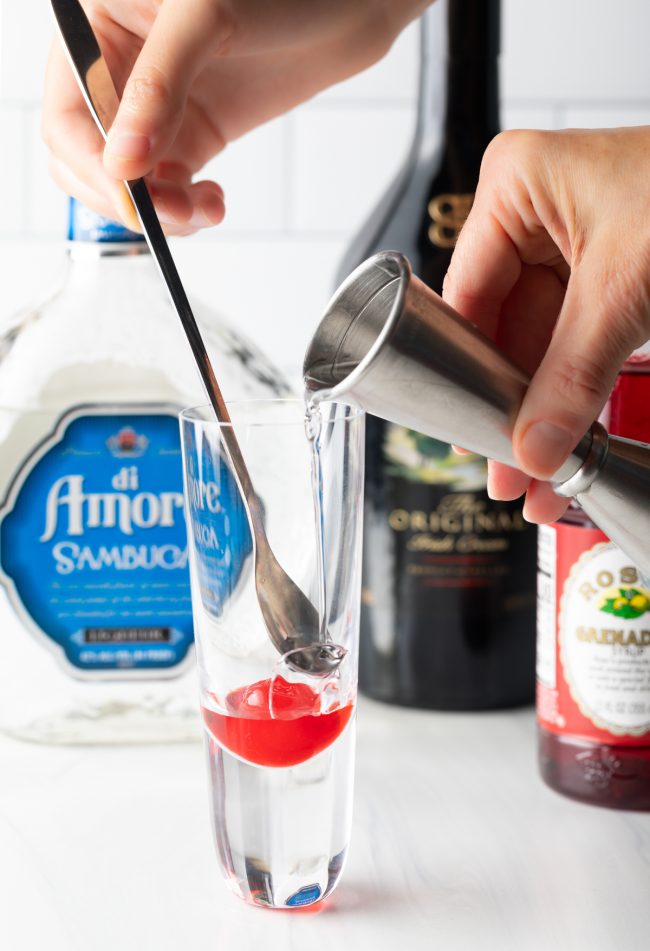 pouring sambuca into shot glass with cherry and grenadine 