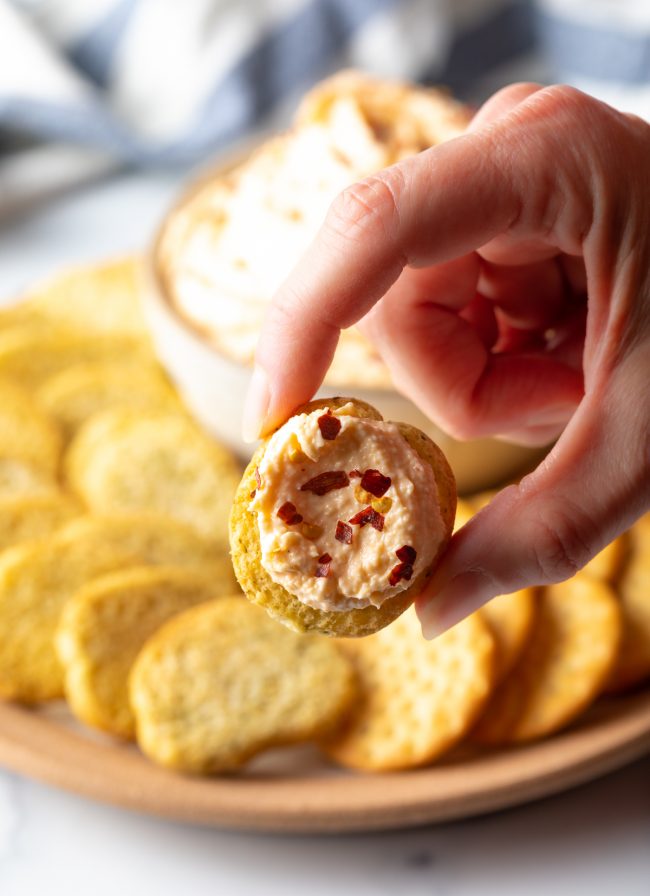 hand holding cracker with smoked gouda spread up to camera